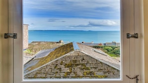 Uitzicht vanuit een raam op een kustgebied met heldere lucht en een rustige zee.