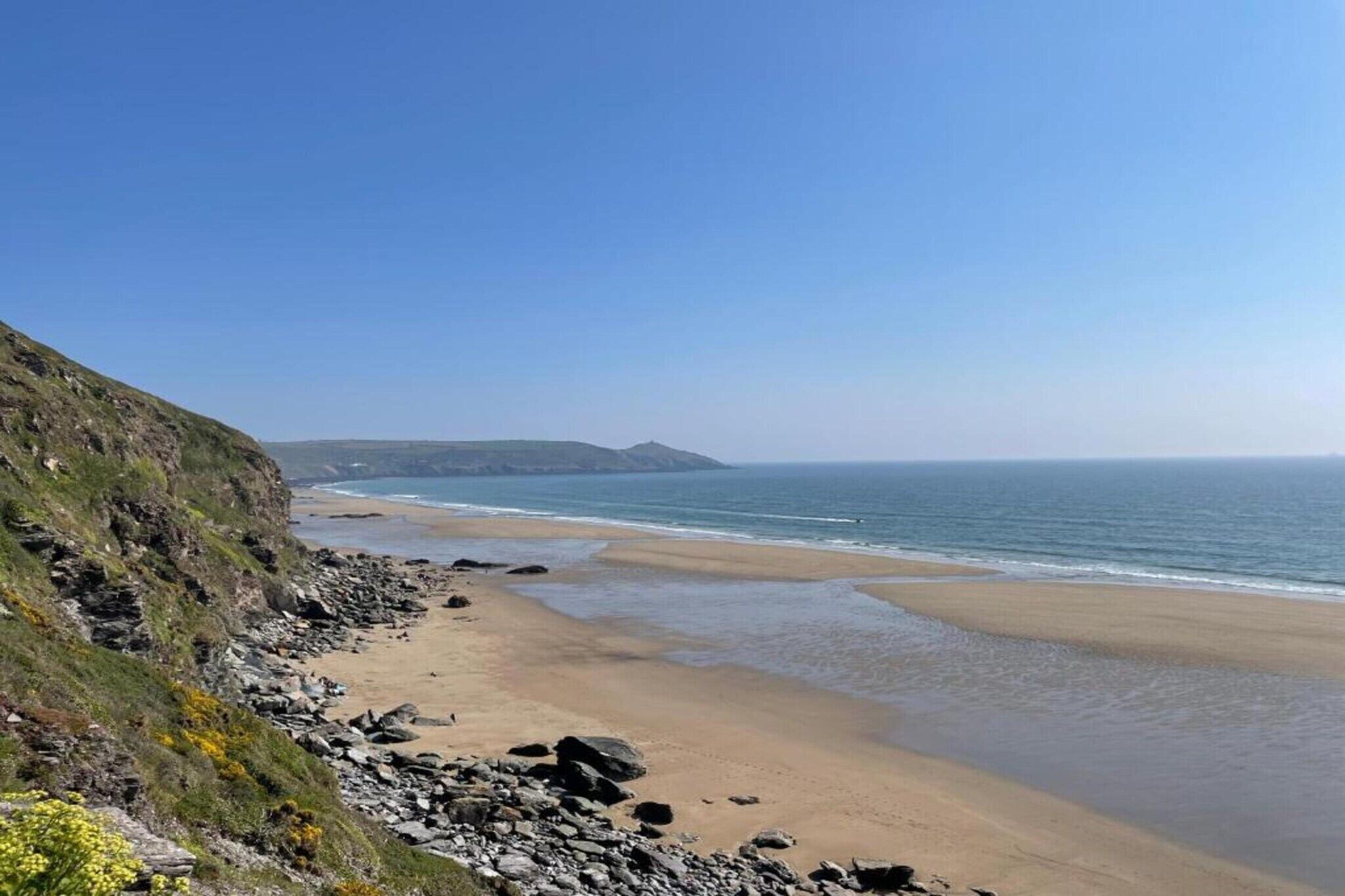 Un paysage côtier avec une plage de sable, des falaises rocheuses et un ciel bleu dégagé.