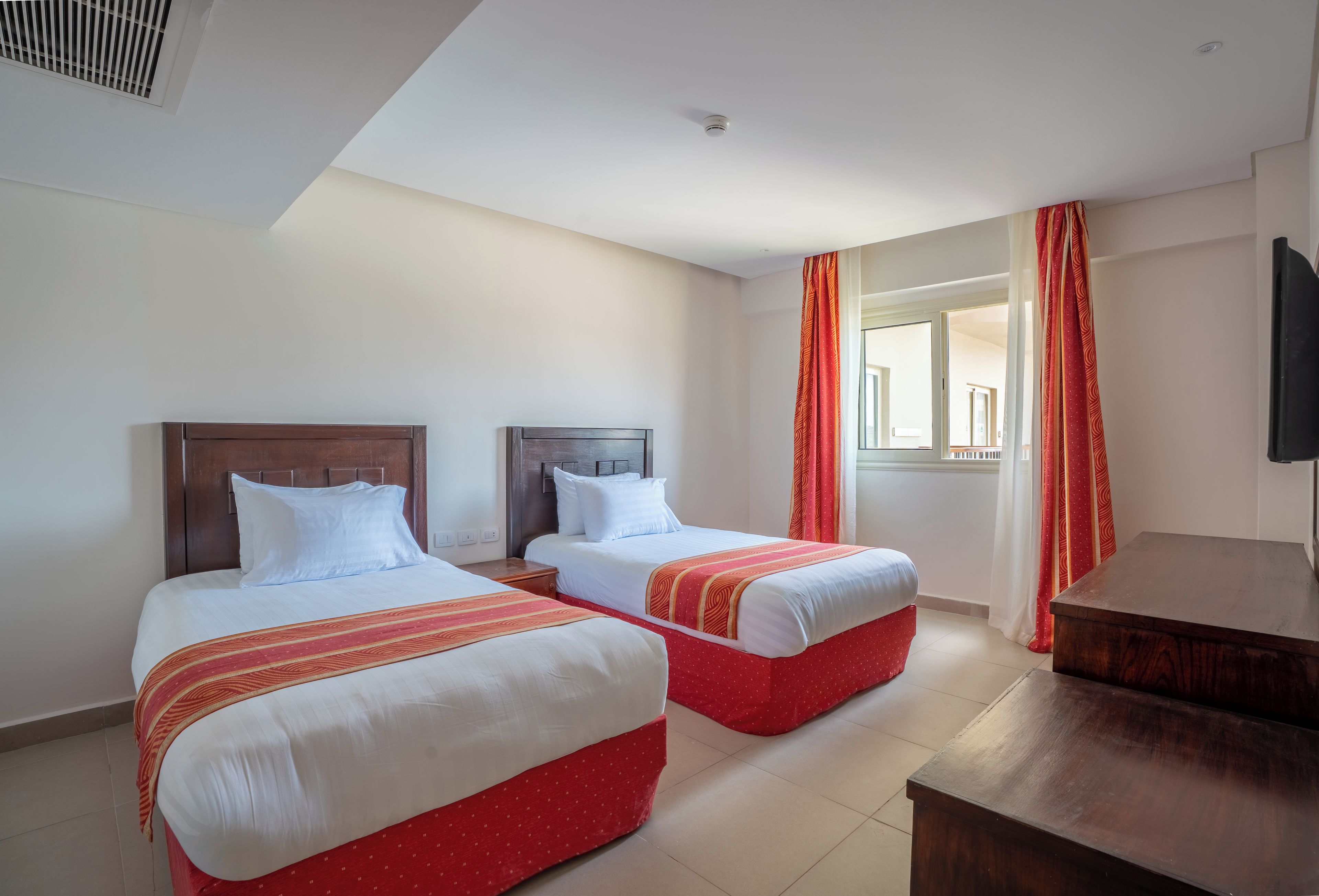 A hotel room with two beds, a wooden headboard, a small wooden table, and a window with curtains.