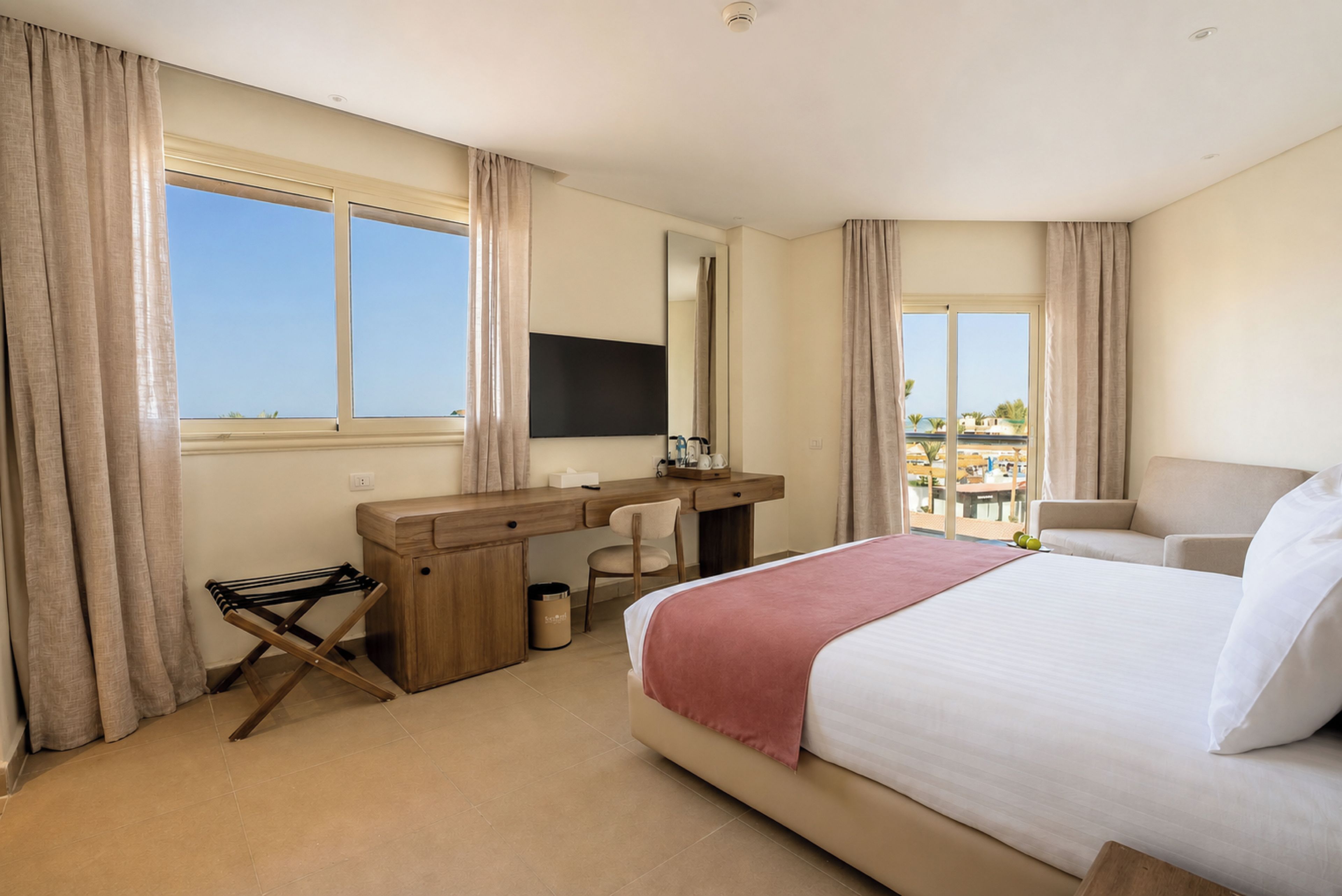 A hotel room with a bed, a desk, a chair, a TV, and a view of the outdoors.