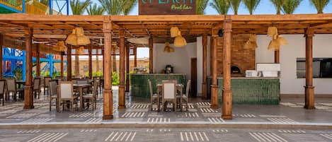 An outdoor pool bar area with wooden pergolas, tables, and chairs.