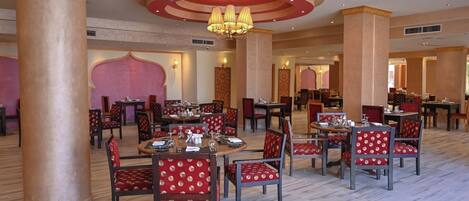 A spacious dining area with multiple tables and chairs, featuring a central chandelier and a marble floor.