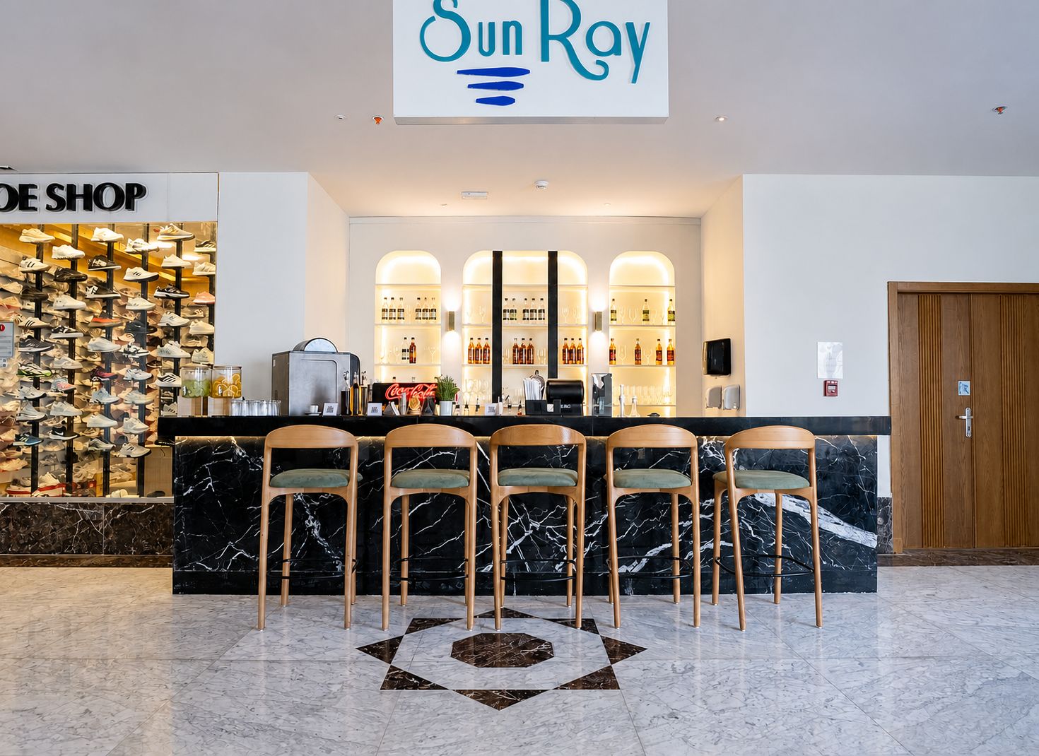 Eine Hotlellobby mit Schuhgeschäft, Barbereich und Rezeption mit Sitzgelegenheiten.