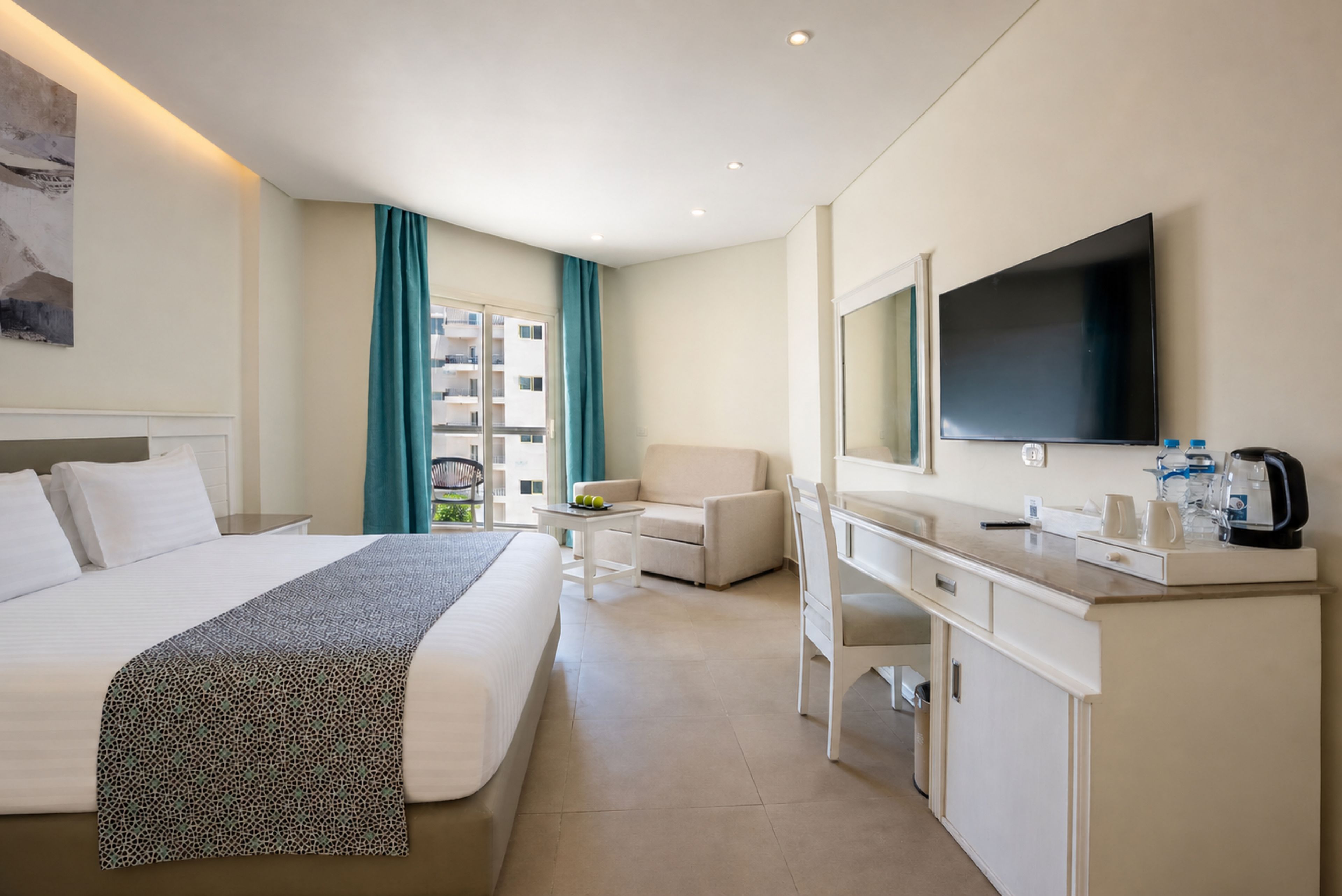 Habitación de hotel con cama, escritorio, silla, televisor y ventana con cortinas.