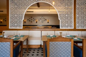 Ein Restaurantinnenraum mit Holztischen, gepolsterten Sitzgelegenheiten, dekorativen Wandverkleidungen und Wandleuchten.