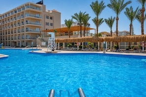 Una piscina con un puesto de salvavidas, sillas de descanso y palmeras.