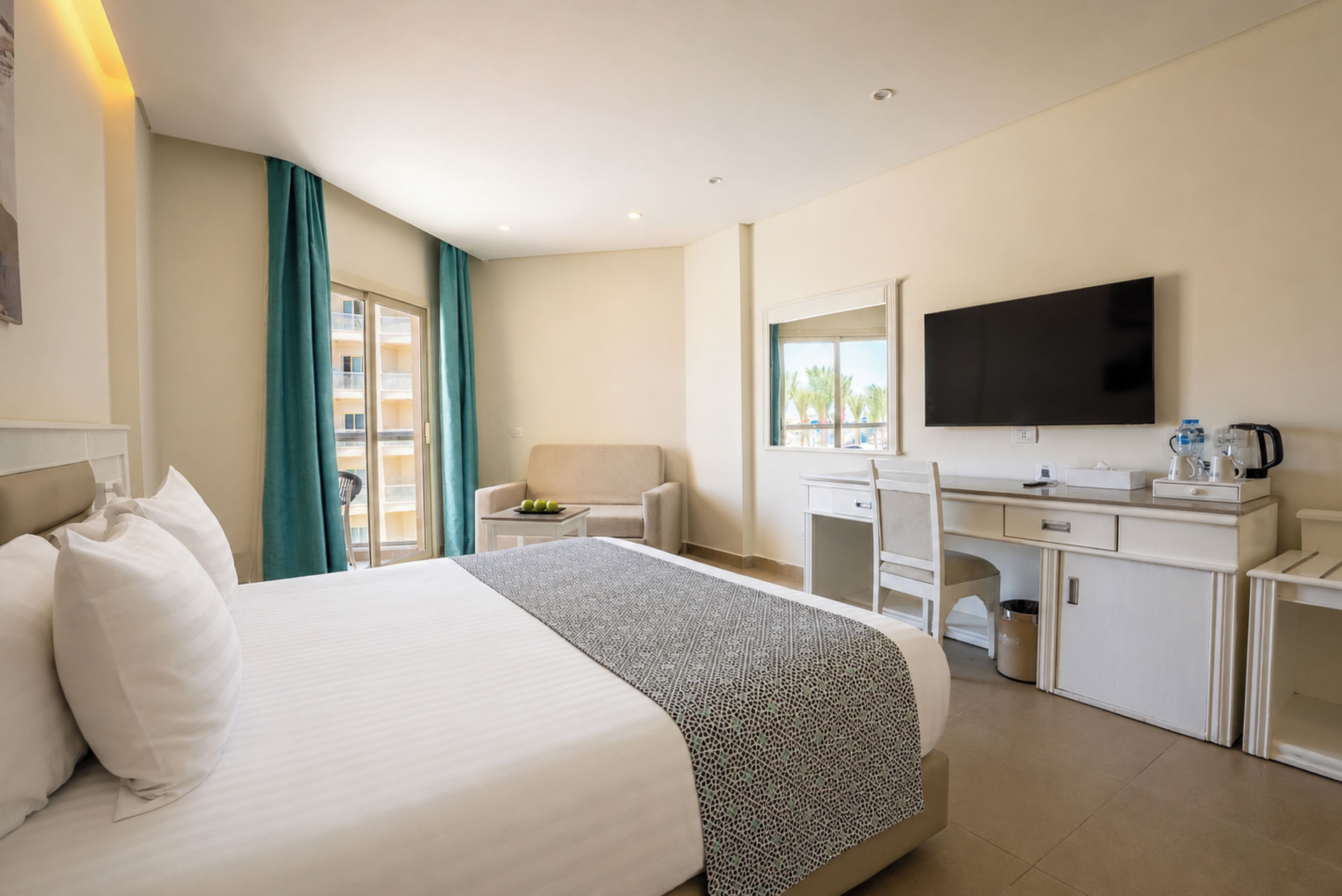Habitación de hotel con cama, escritorio, silla, televisor y ventana con cortinas.