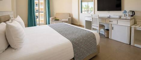 Habitación de hotel con cama, escritorio, silla, televisor y ventana con cortinas.