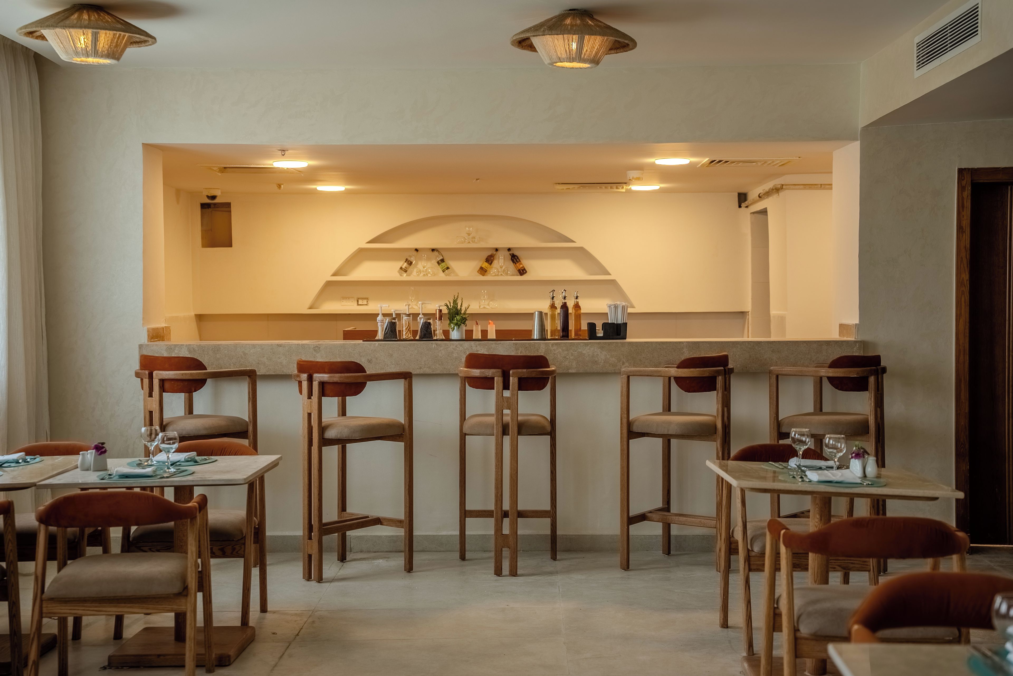 Ein Restaurant mit hohen Holzhocker, Tischen mit Stühlen und einer Theke mit Flaschen und Gläsern.