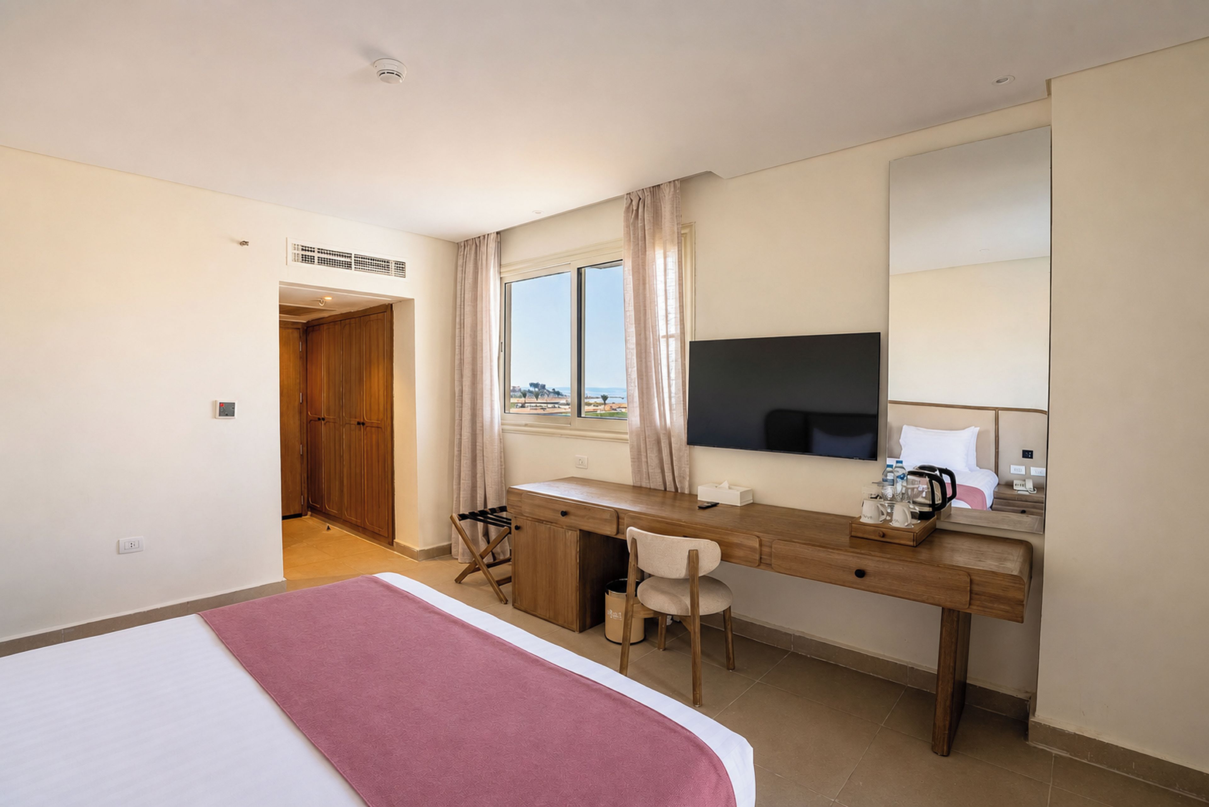 A hotel room with a bed, a desk, a chair, a television, and a window with a view.
