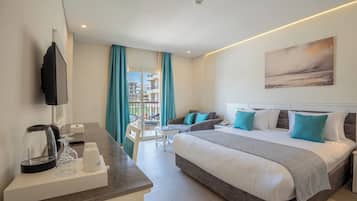 Habitación de hotel con cama, escritorio con hervidor y vasos, una silla, y vista a edificios a través del ventanal.