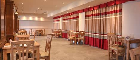 A spacious dining area with wooden tables and chairs, red and white curtains, and recessed ceiling lighting.