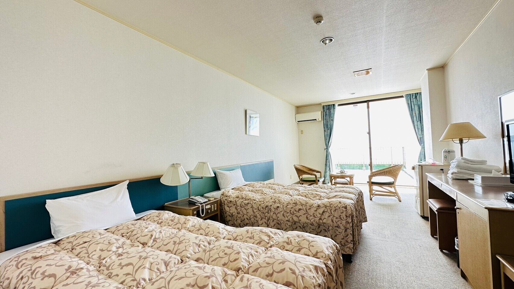 Habitación de hotel con dos camas, un escritorio, una silla, una mesita y un balcón con vistas.