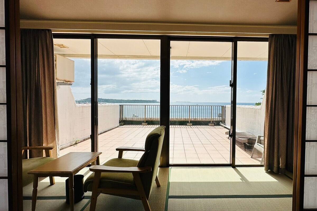 A room with a sliding glass door leading to a balcony with a view of the sea.