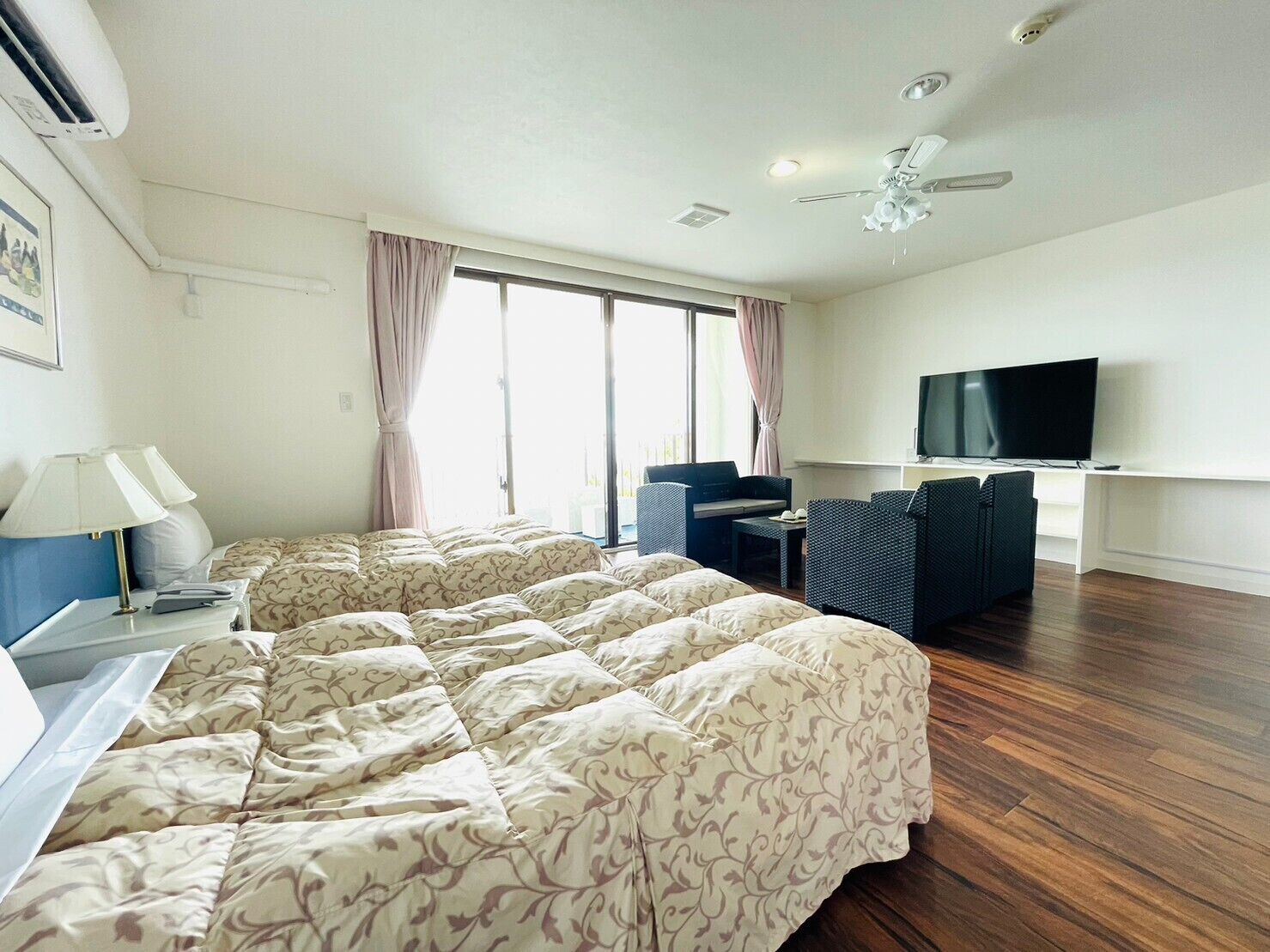 Una habitación de hotel con cama, escritorio, silla, televisión y ventana con cortinas.