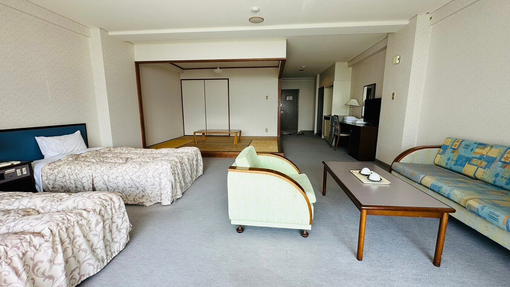 Habitación de hotel con dos camas individuales, un sofá, una mesita y un televisor.