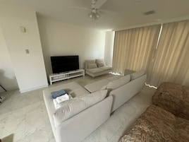 Una sala de estar moderna con un sofá blanco grande, un televisor de pantalla plana sobre un mueble blanco y un ventilador de techo.