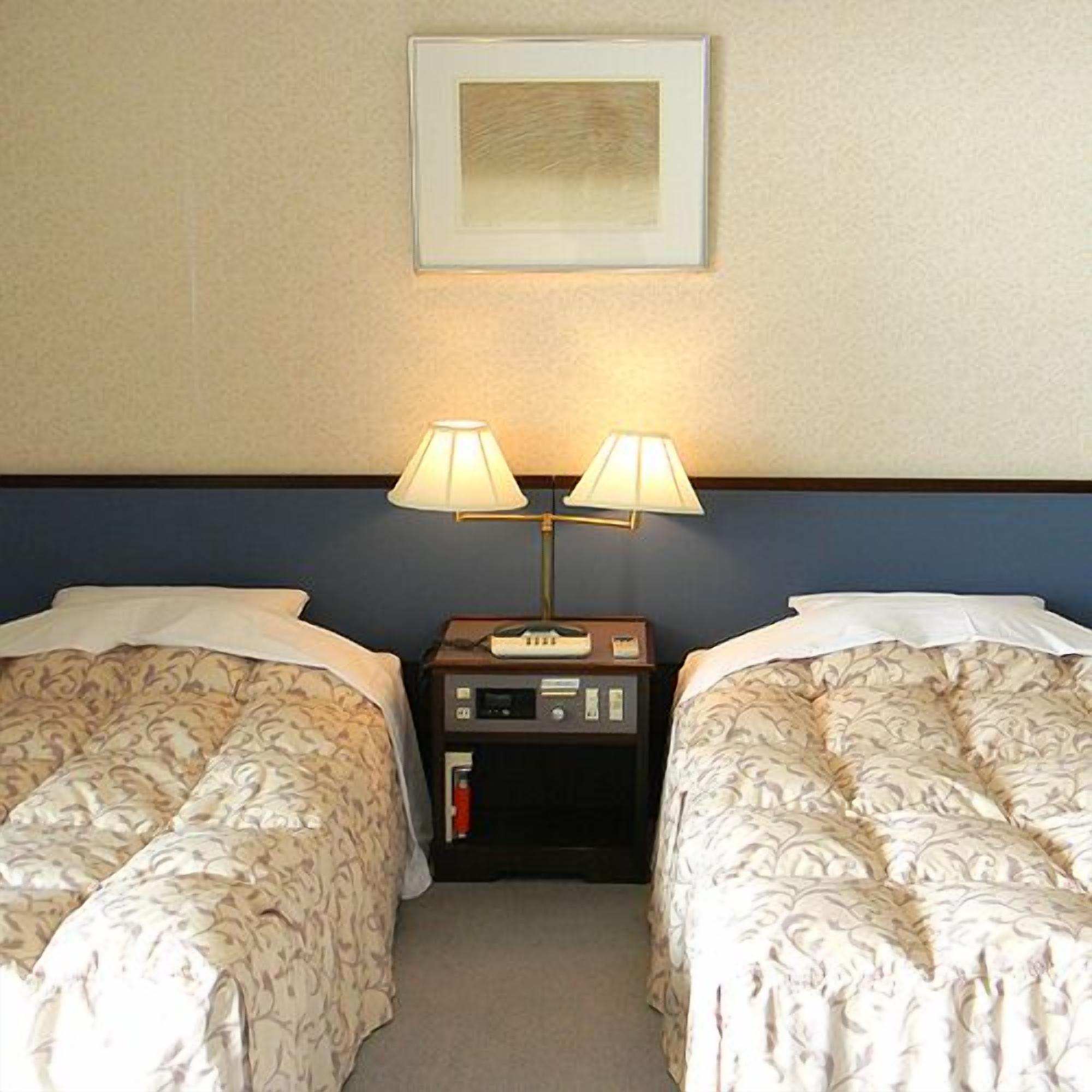 Et hotelværelse med to senge, et natbord med en lampe og et billede i ramme på væggen.