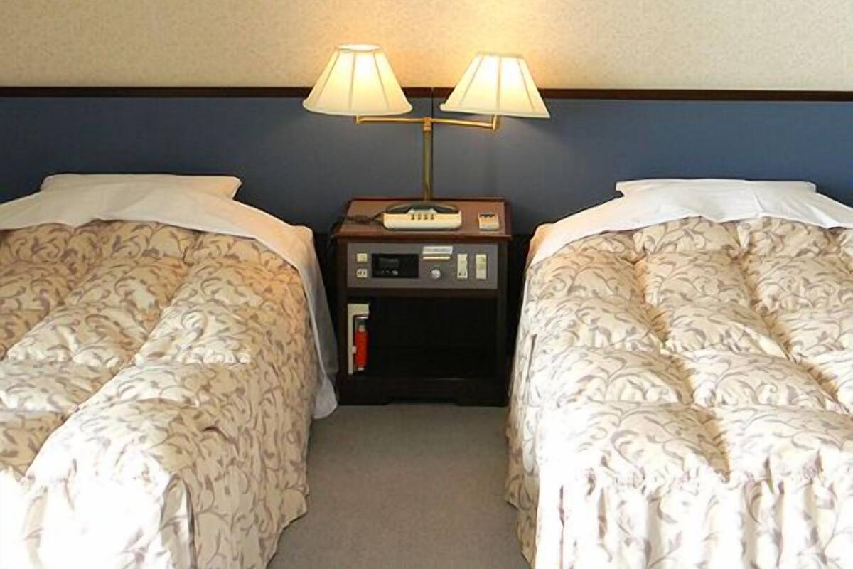 A hotel room with two beds, a nightstand with a lamp, and a framed picture on the wall.