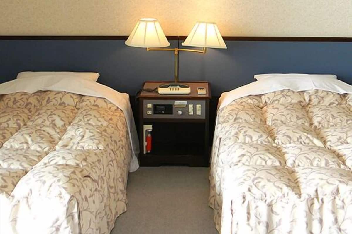 A hotel room with two beds, a nightstand with a lamp, and a framed picture on the wall.