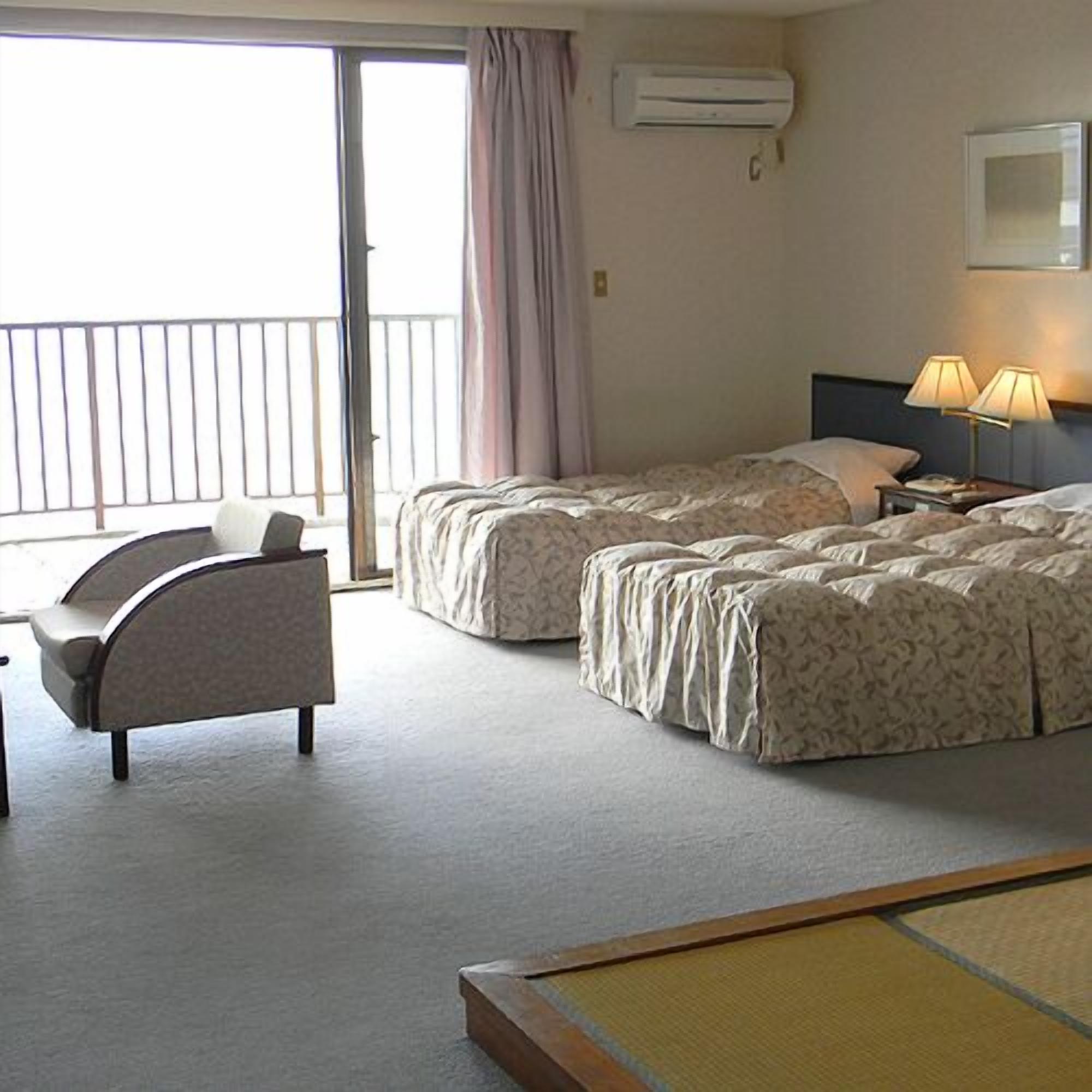Habitación de hotel con dos camas, una silla, equipo de aire acondicionado, lámpara y vista al exterior.