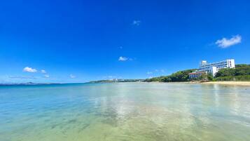 A coastal view with clear water, a beach, and a building with multiple floors.