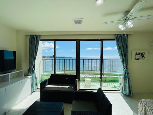Un balcón con vista al mar, un televisor a la izquierda y un ventilador de techo.