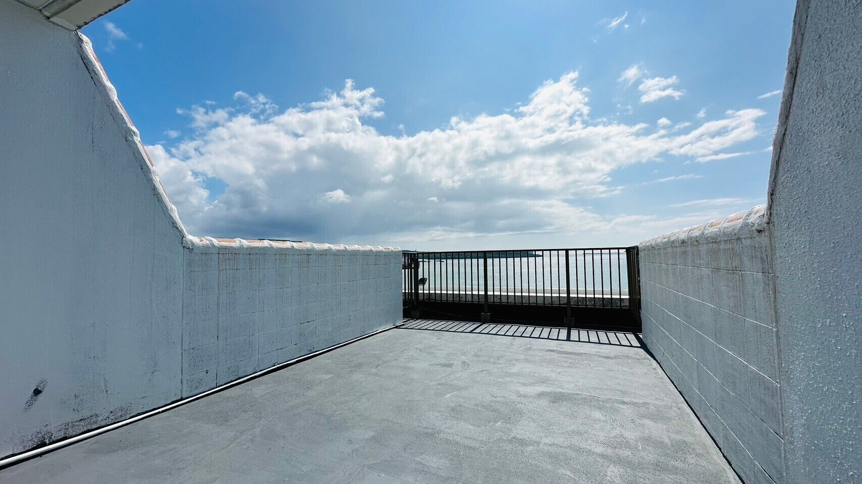 Terraza en la azotea con barandilla de metal, suelo de hormigón y cielo despejado.