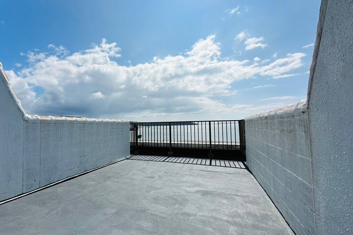 A rooftop terrace with a metal railing, concrete floor, and a clear sky.