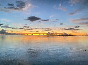 Água calma com margem distante e céu ao pôr do sol.