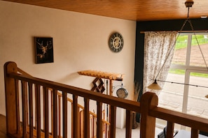 A wooden staircase leading to a room with a clock, a framed deer picture, and a window with a view of the outside.