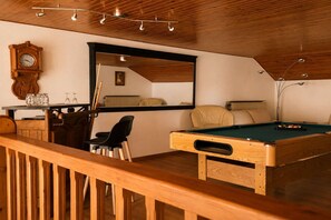 Una mesa de billar con estructura de madera, un reloj y un espejo en la pared.