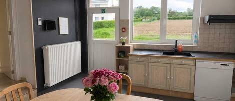 A kitchen with a dining table, a vase of flowers, a window with a view of a field, and a dishwasher.