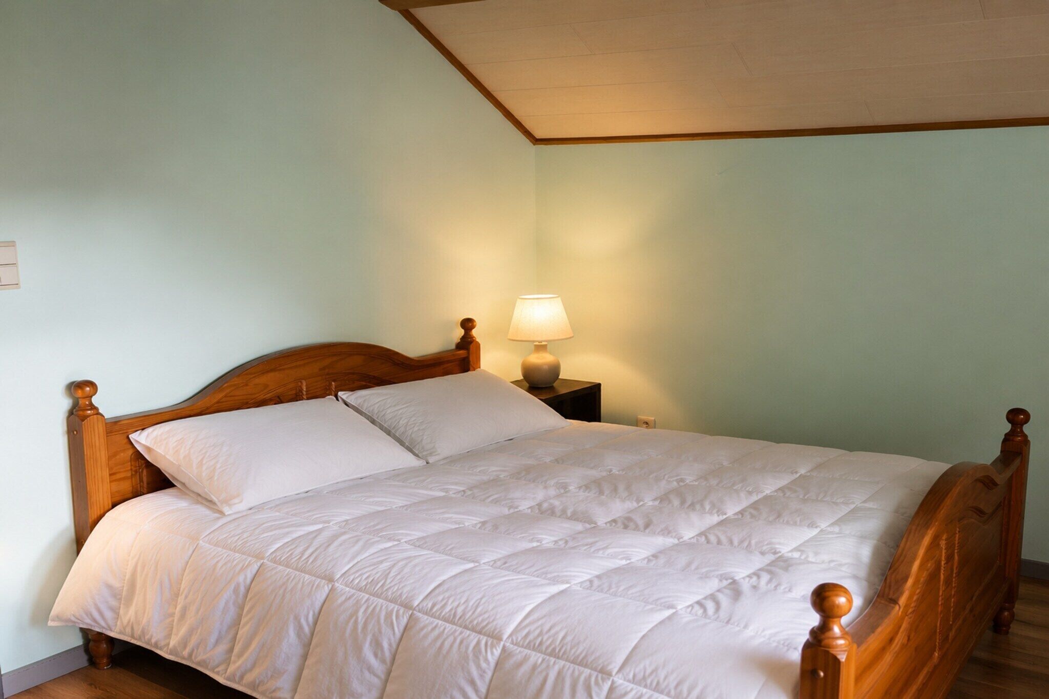 A neatly made bed with a wooden headboard, a bedside lamp, and a nightstand.