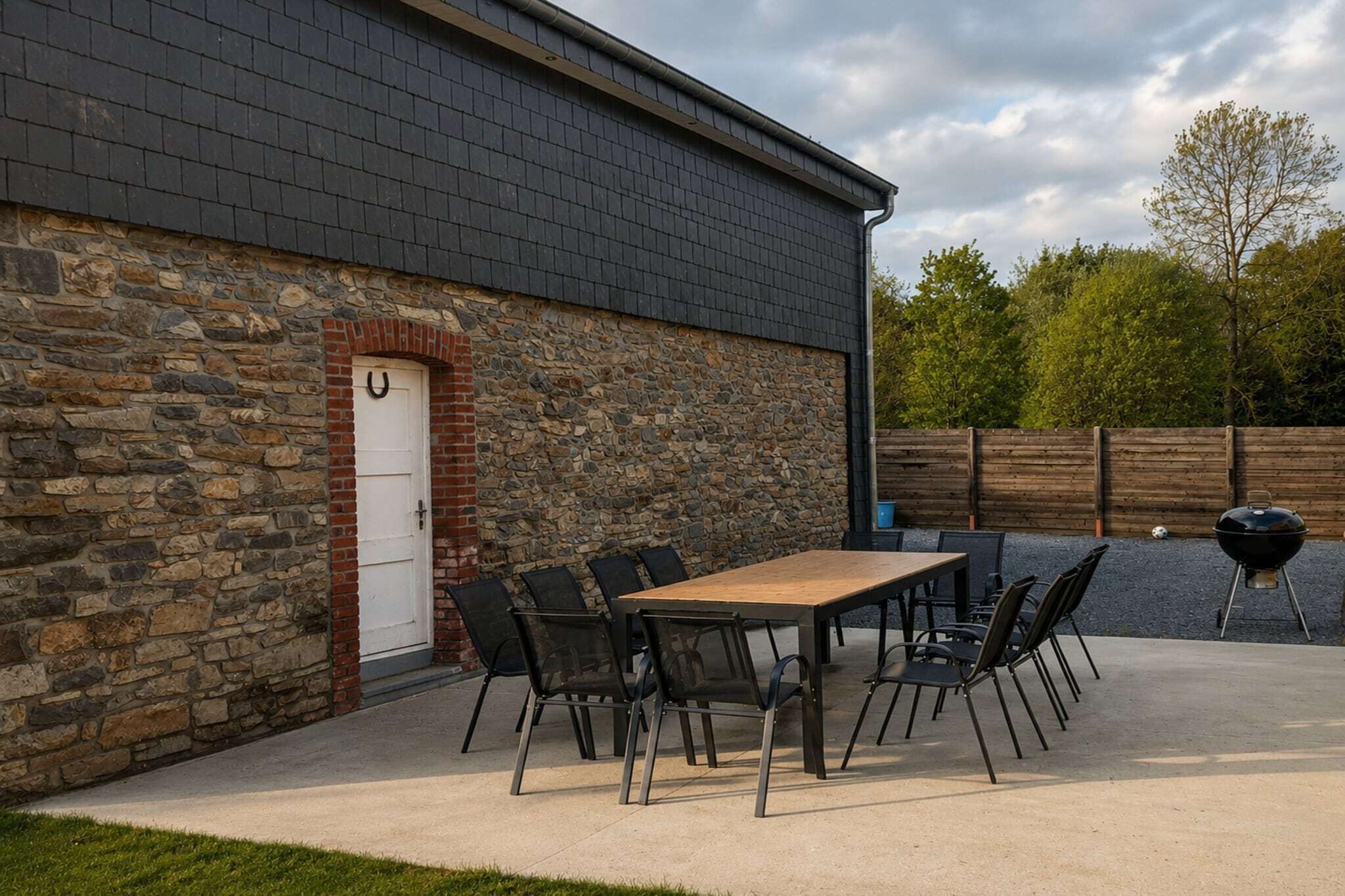 A stone building with a dark roof, a white door, and a patio with a table and chairs.