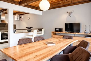 A modern kitchen with built-in appliances, a dining area with a wooden table and cushioned chairs, and a mounted television.