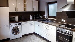 A modern kitchen with white cabinets, a built-in washing machine, a microwave, a coffee maker, and a stove.