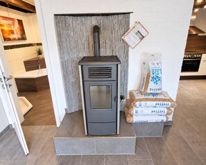 A modern kitchen with a built-in wood stove, a stone accent wall, and a view of the living area.