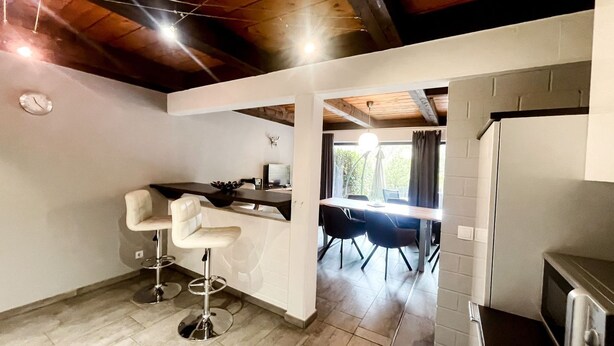 A modern kitchen with white cabinets, a dining area with a table and chairs, and a bar stool.