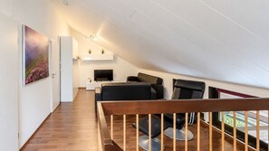 A modern living room with a sloped ceiling, a flat-screen TV, a sofa, and a coffee table.