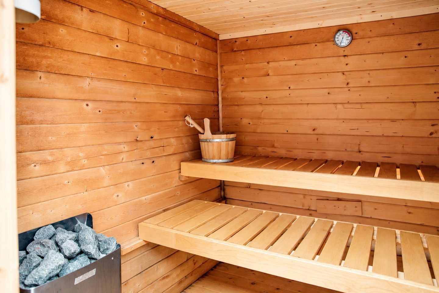 Un sauna en bois avec des bancs et un seau rempli de pierres.
