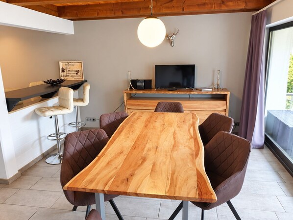 A modern dining area with a wooden table and leather chairs, a bar with a white countertop, and a television on a wooden stand.