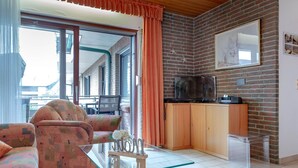 A living room with a sofa, a glass coffee table, and a TV on a wooden cabinet. - Coffee, cake and the smell of the coast (Sylt)