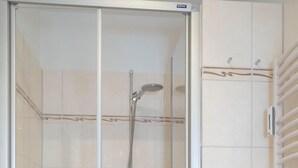 A modern bathroom with a glass-enclosed shower, a white toilet, and a towel rack. - Coffee, cake and the smell of the coast (Sylt)