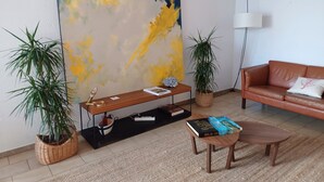 Ein Wohnzimmer mit einem großen abstrakten Gemälde, zwei Topfpflanzen, einem Ledersofa, einem Couchtisch und einem Bücherregal.