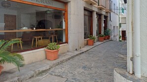 Ein Restaurant mit großen Glasschaufenstern, Außenbestuhlung und Pflanzen in Töpfen entlang des Gehwegs.