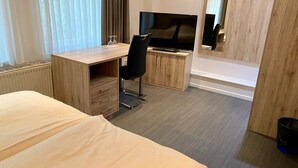 Une chambre d’hôtel avec un lit, un bureau et une chaise, une télévision et une petite fenêtre avec des rideaux.
