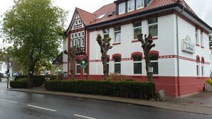 Un bâtiment à deux étages avec une façade rouge et blanche, une enseigne verte indiquant un restaurant, et une route dégagée devant.
