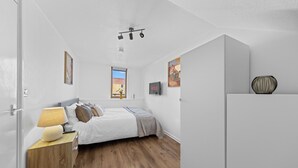 Un dormitorio con cama, mesita de noche, lámpara y televisión en la pared.