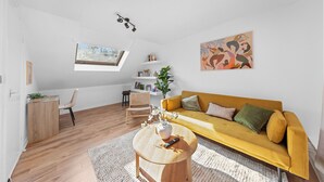 Una sala de estar moderna con un sofá amarillo, una mesa de centro de madera, una pared blanca con un cuadro y un tragaluz.